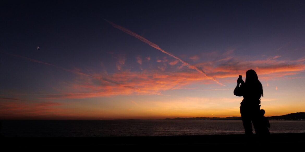 a person taking a picture of a sunset with a cell phone