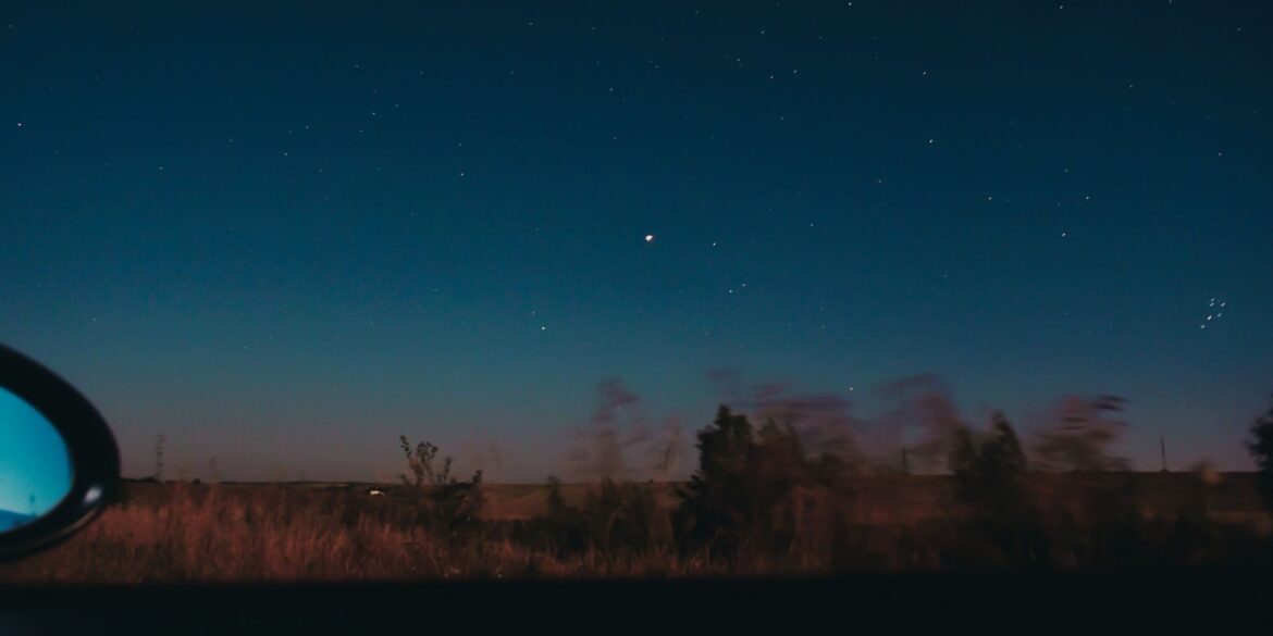 View through moving car window of horizon line with dark star sky and blurred trees