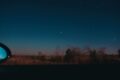 View through moving car window of horizon line with dark star sky and blurred trees