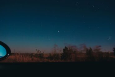 View through moving car window of horizon line with dark star sky and blurred trees